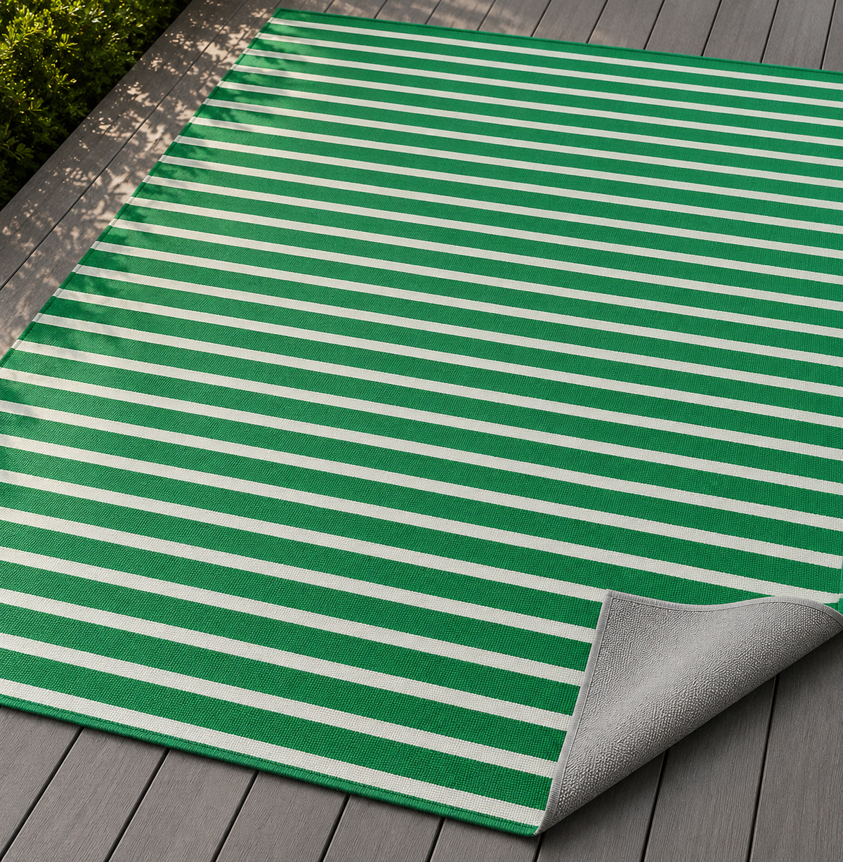 Green and white striped outdoor rug with the corner folded back — matte grey non-slip backing