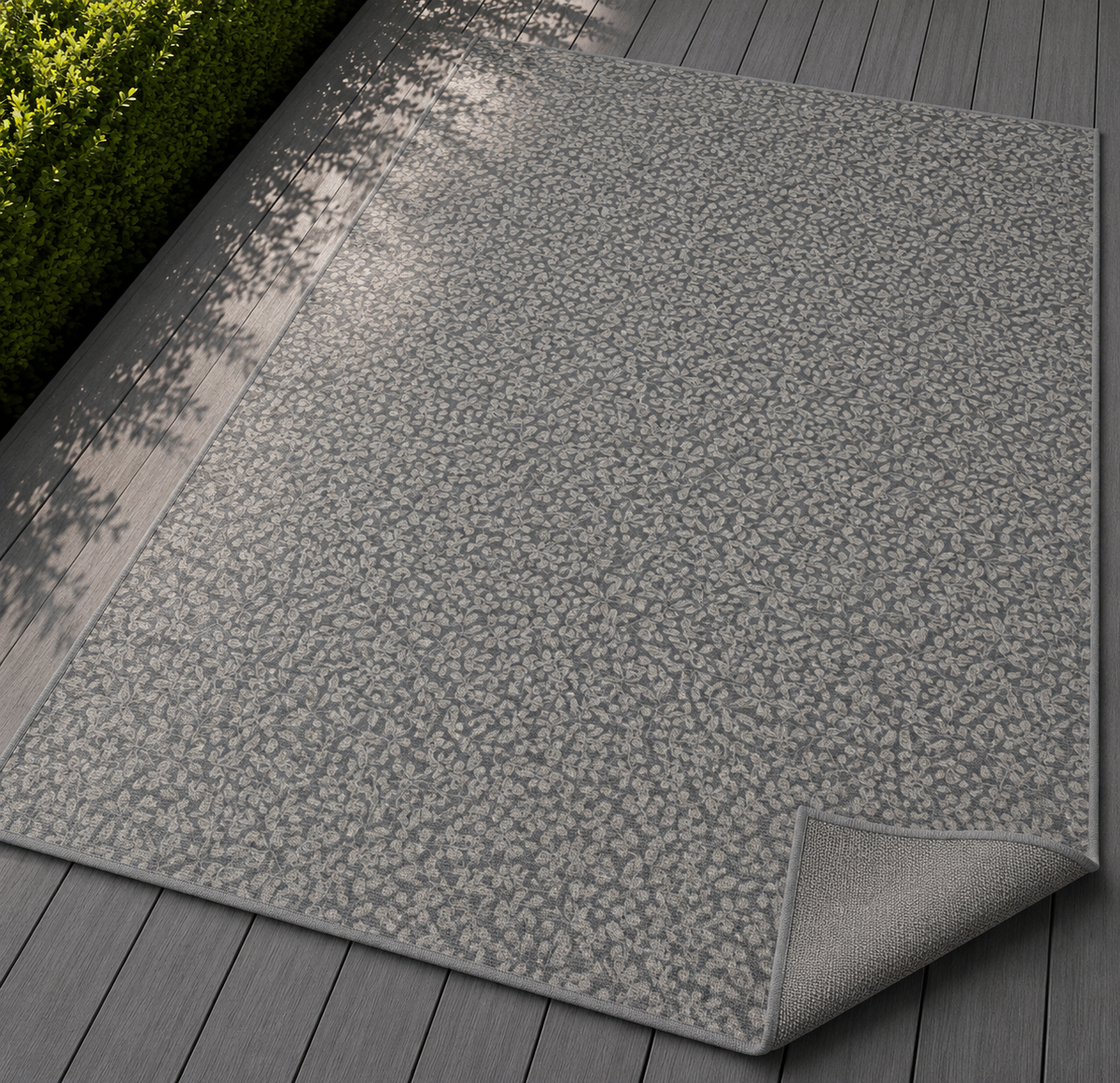 Grey foliage outdoor rug with the corner folded back — matte grey non-slip backing