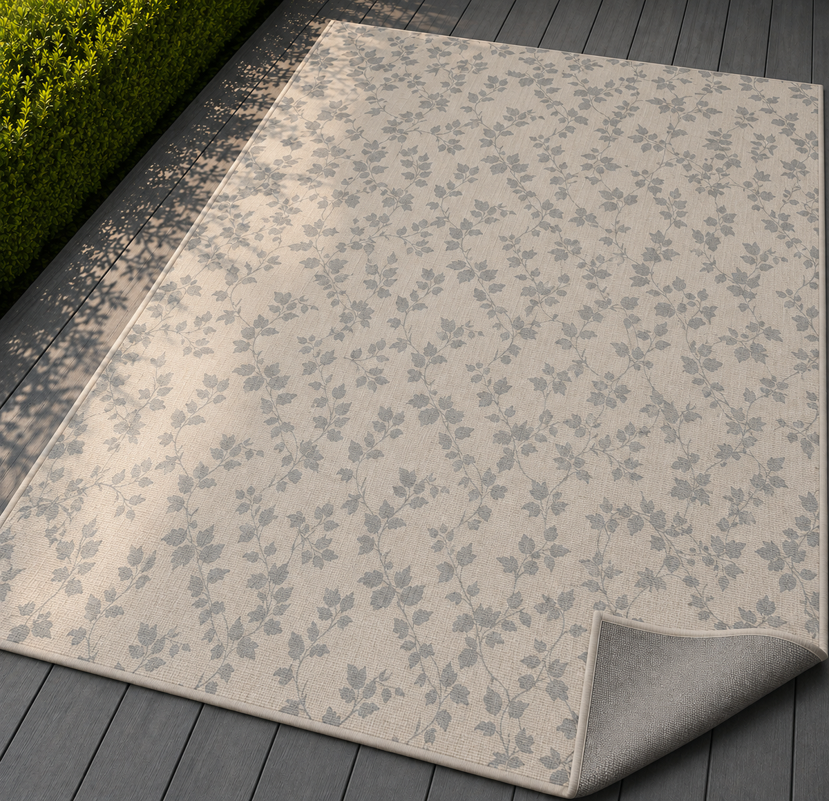 Grey trailing vine outdoor rug with the corner folded back — matte grey non-slip backing