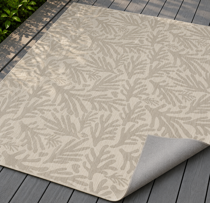 Neutral coral branch outdoor rug with the corner folded back — matte grey non-slip backing