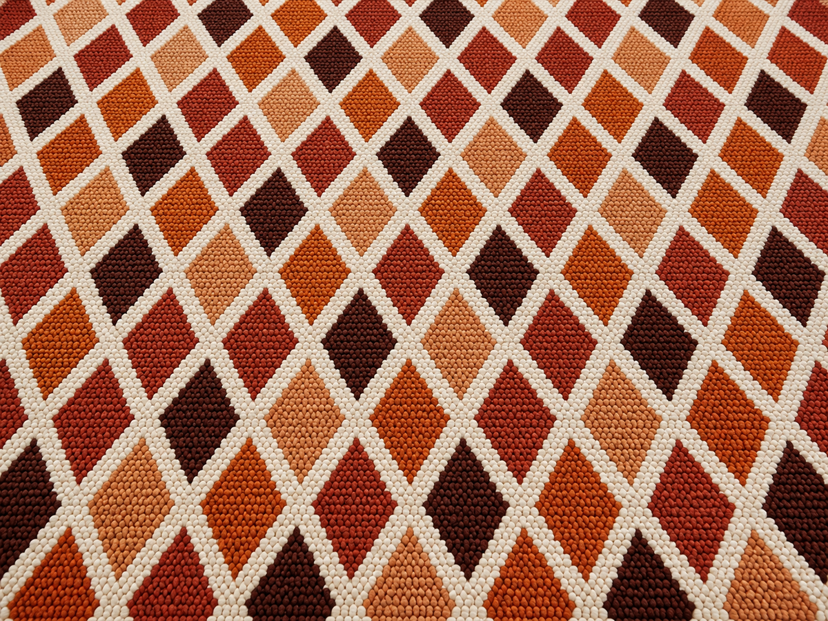 Close-up of the rust harlequin diamond outdoor rug — short, dense low-pile chenille nap
