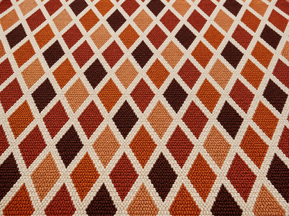 Close-up of the rust harlequin diamond outdoor rug — short, dense low-pile chenille nap