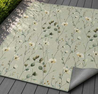 Sage wildflower outdoor rug with the corner folded back — matte grey non-slip backing